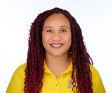 smiling woman with tan skin and long, dark reddish braided hair, wearing a bright yellow polo shirt